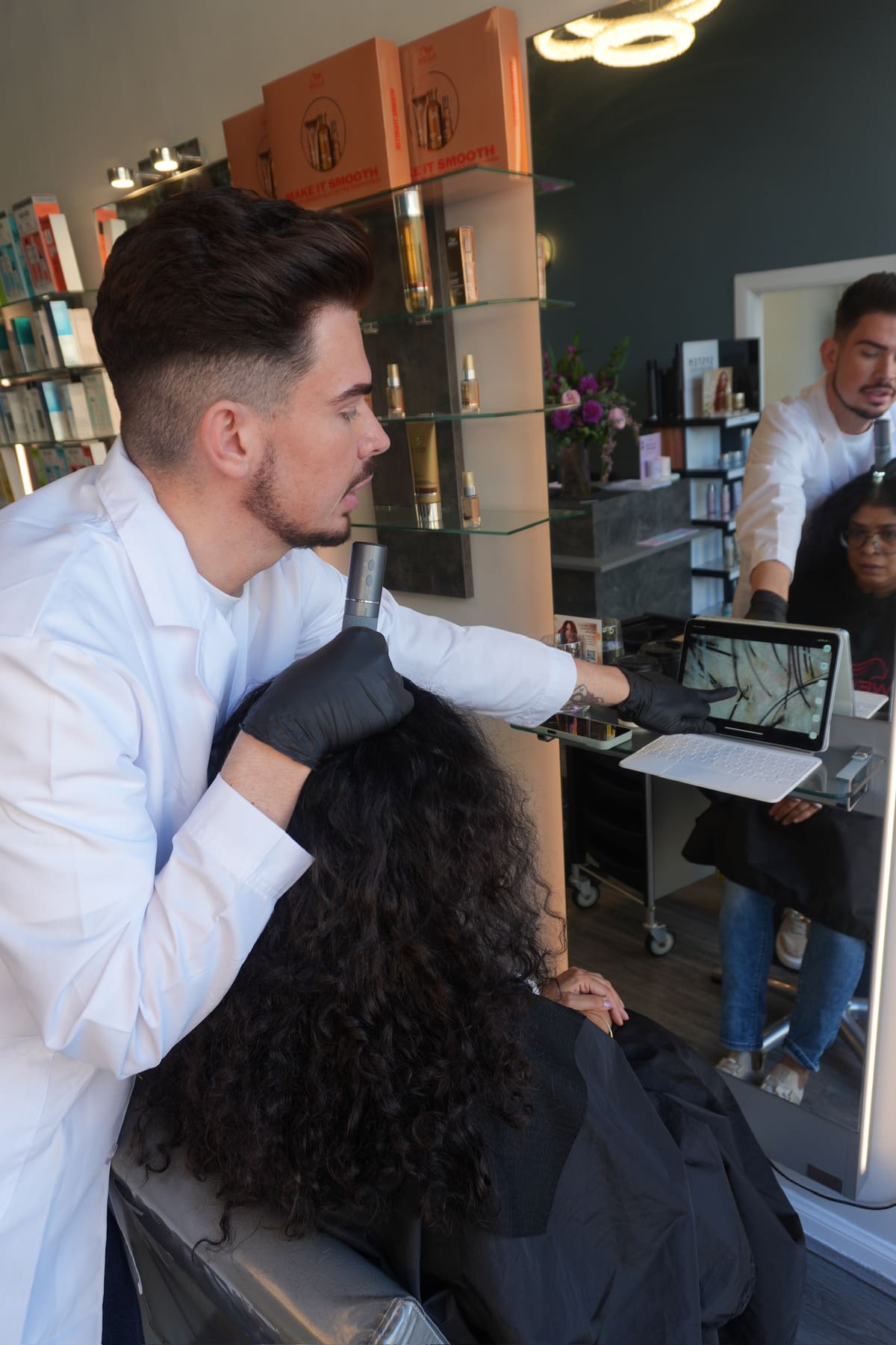 A scalp being examined with a digital microscope, the magnified image on a tablet beside it